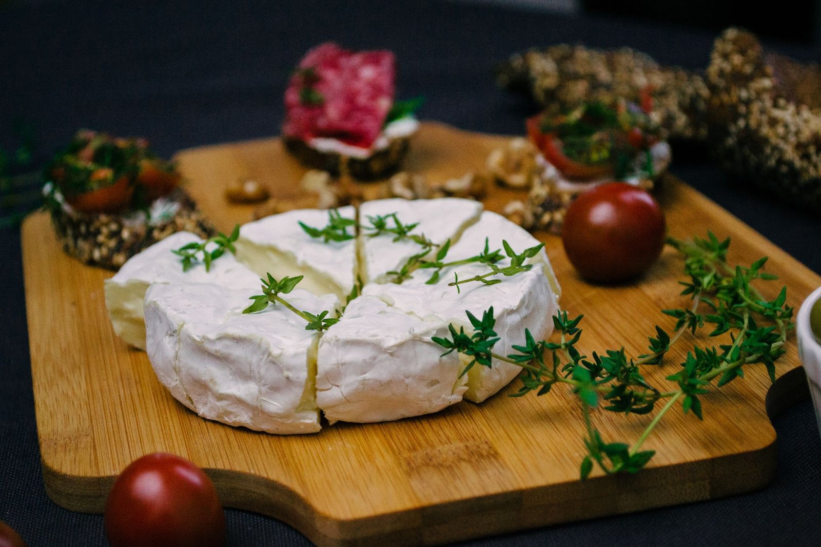 Formaggio fresco con rametti di timo su un tagliere di legno, con del salume sullo sfondo