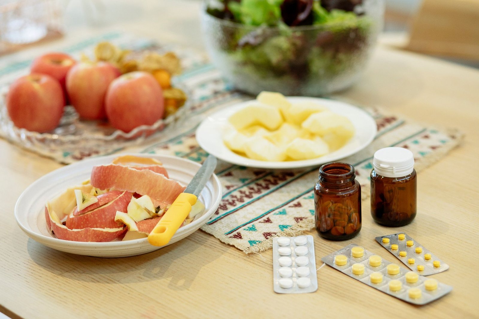 Tavolo di cucina con mele, un'insalata e boccette di integratori con i blister