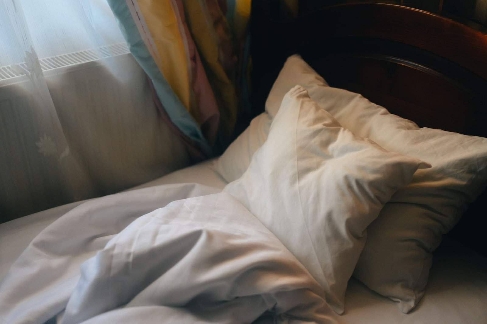 Due cuscini appoggiati alla testata di legno di un letto sfatto, luce calda del mattino