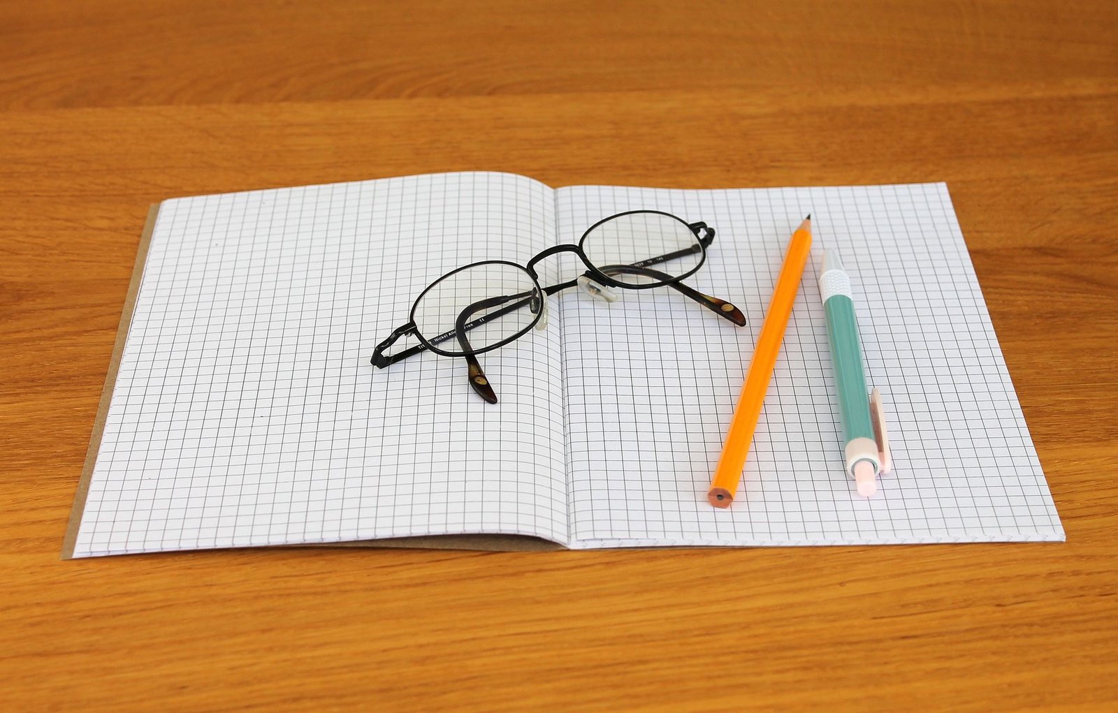 Un quaderno aperto con occhiali da lettura e matite, su un tavolo di legno