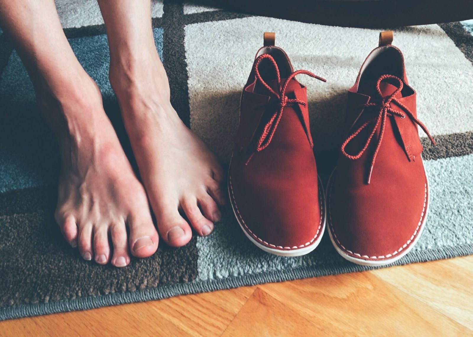 Piedi scalzi accanto a un paio di scarpe comode, su un tappeto di casa