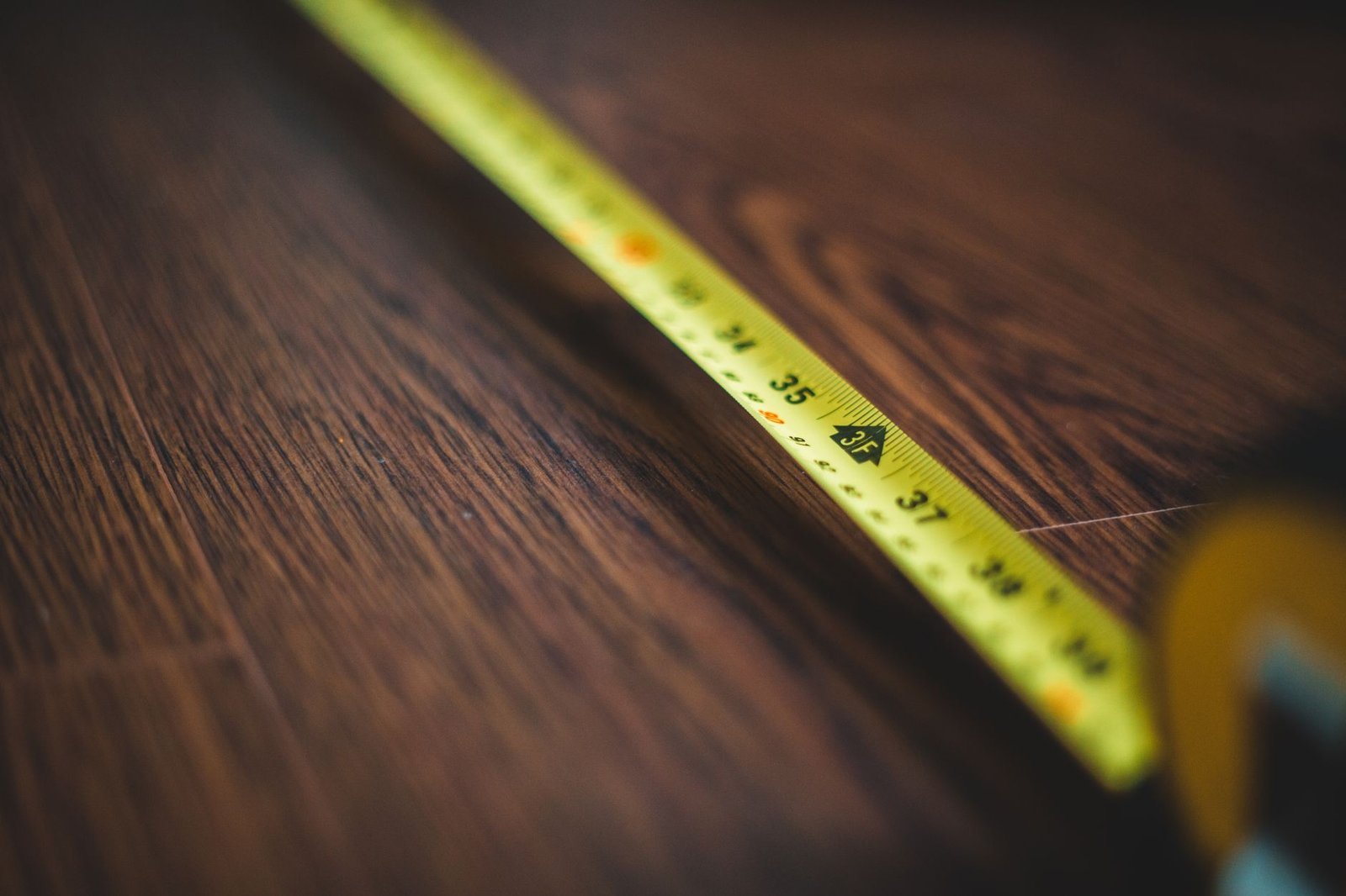 Un metro da sarta giallo disteso su un pavimento di legno scuro, i centimetri ben leggibili