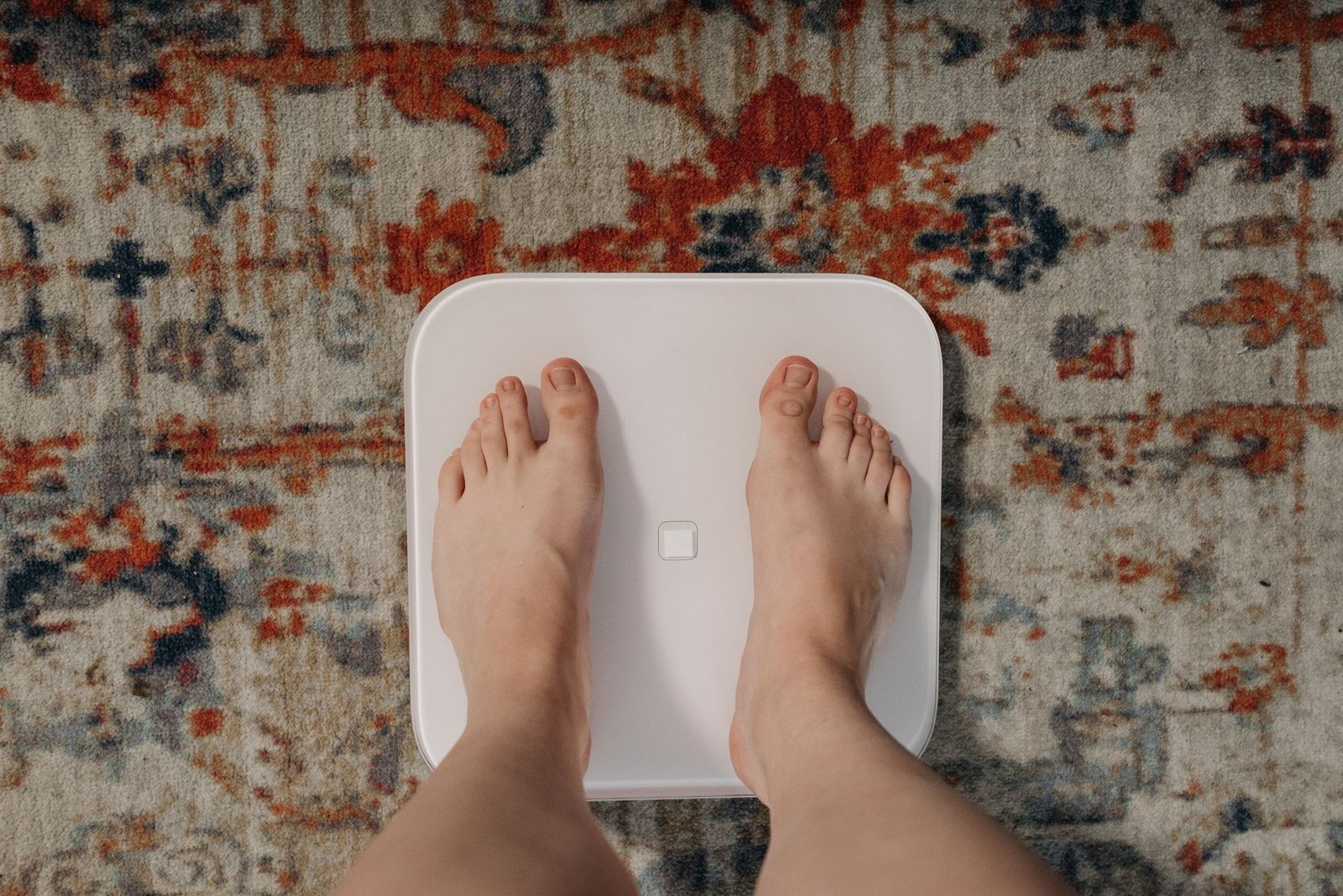 Piedi su una bilancia digitale bianca, sul tappeto del bagno di casa