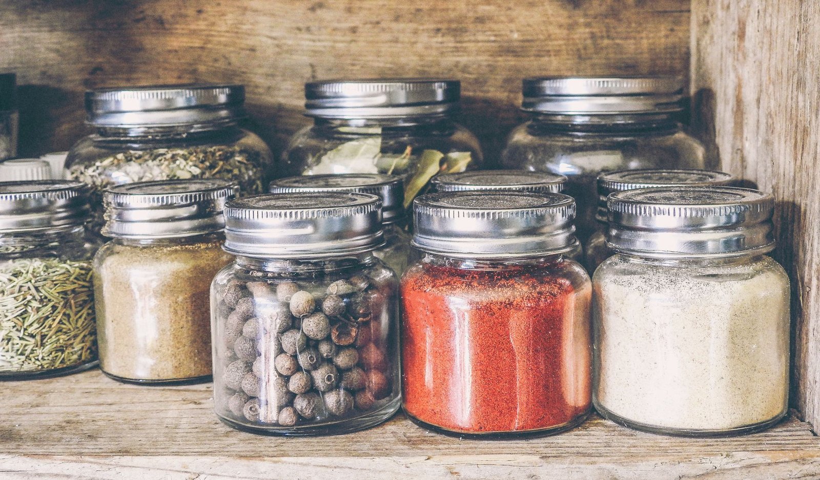 Barattoli di vetro con spezie ed erbe aromatiche su una mensola di legno in cucina