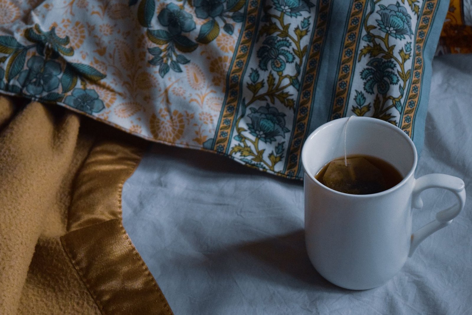 Una tazza di tisana calda appoggiata sul letto tra le coperte, di sera