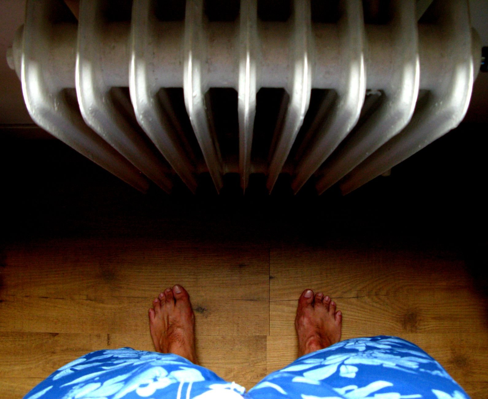 Due piedi scalzi affiancati sul pavimento di legno, visti dall'alto, vicino al termosifone