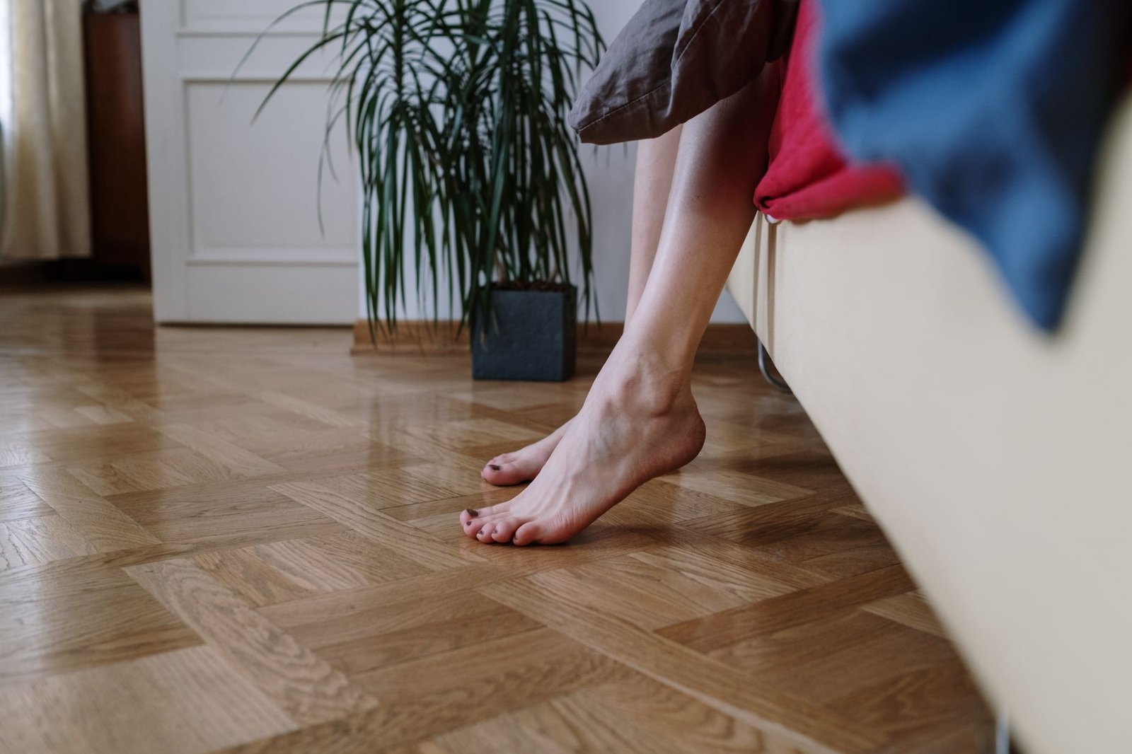 Una gamba scende verso il pavimento di legno accanto al divano, una pianta sullo sfondo, a casa